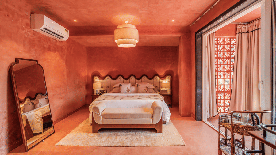 Bedroom at Unseen Boutique Hotel with reddish?orange walls, scalloped headboard, white bedding, pendant ceiling light, large mirror, and sliding door to balcony.