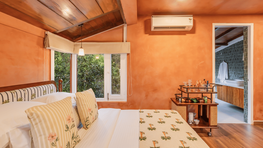 View of the Penthouse at Unseen Boutique Hotel Assagao Goa with a king bed, terracotta walls, wooden ceiling, and an attached bathroom beyond.
