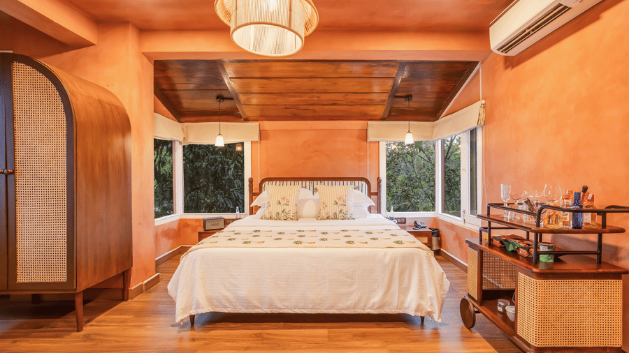 View of the Penthouse at Unseen Boutique Hotel Assagao Goa with a king bed, rattan pendant light, wooden ceiling, and warm natural light.