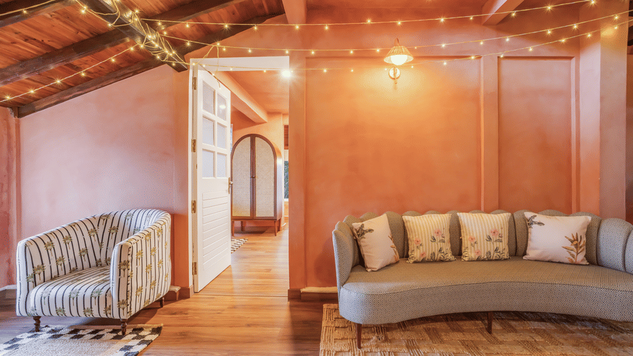 View of the Penthouse living area at Unseen Boutique Hotel Assagao Goa with a curved sofa, armchair, fairy lights, and warm ambient lighting.