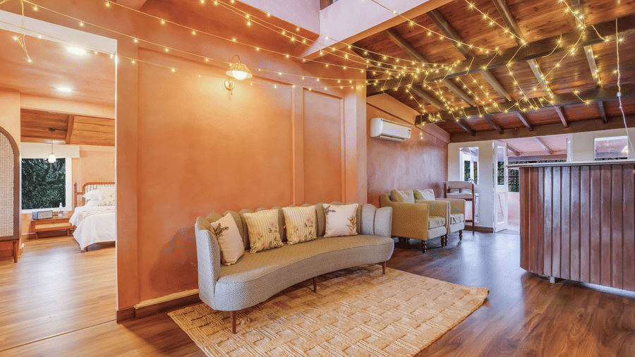 Wide view of the Penthouse living area at Unseen Boutique Hotel Assagao Goa with a curved sofa, fairy lights, wooden flooring, and warm ambient lighting.