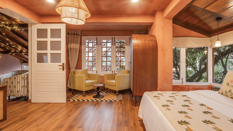Wide view of the Penthouse at Unseen Boutique Hotel Assagao Goa with twin beds, rattan pendant light, terracotta walls, and wooden flooring.