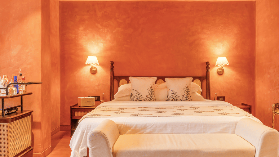 Bedroom at Unseen Boutique Hotel with orange walls, white bedding, cushioned bench, and soft lighting creating a welcoming and comfortable ambience.