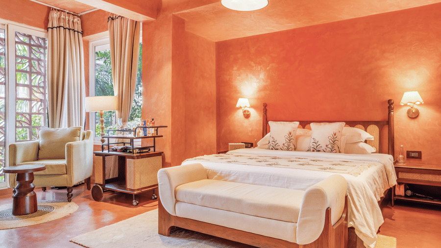 Vibrant bedroom at Unseen Boutique Hotel with bold orange walls, large bed, and natural light creating a lively yet welcoming ambience.