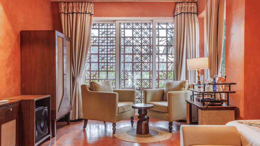 Living room at Unseen Boutique Hotel with orange walls, beige armchairs around a wooden table, and warm lighting creating a cosy and elegant atmosphere.