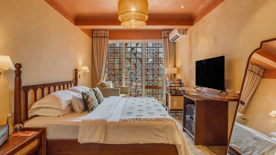 Bedroom at Unseen Boutique Hotel featuring wooden desk, TV, patterned bedspread, bedside lamps, and warm wall accents.
