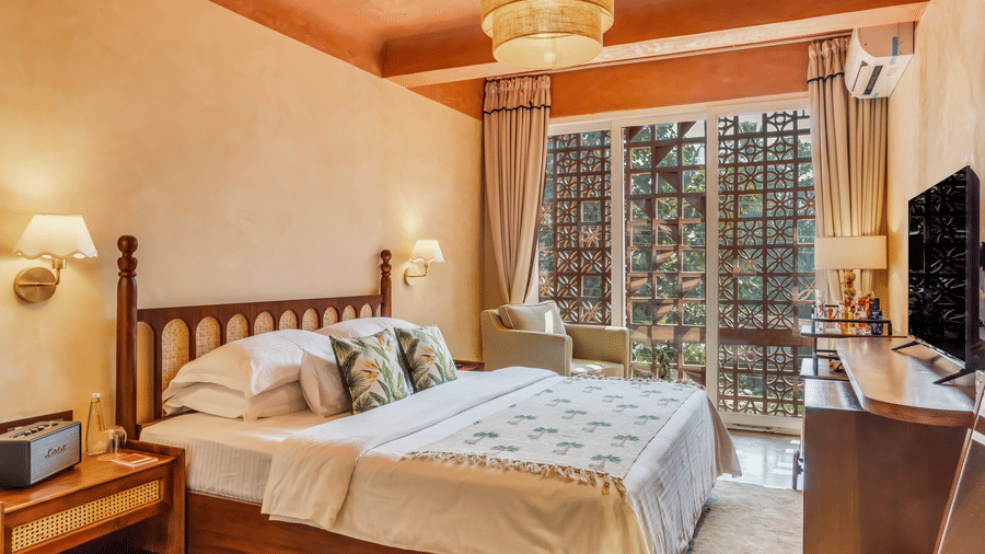 Bedroom at Unseen Boutique Hotel with wooden bed, white and green bedding, bedside lamps, window with curtains, and ceiling light fixture.