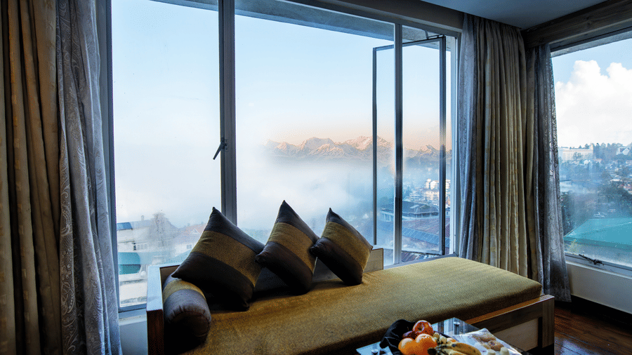 Executive room seating area with cushioned bench, fruit table, and misty mountain view at Viceroy Hotel, Darjeeling