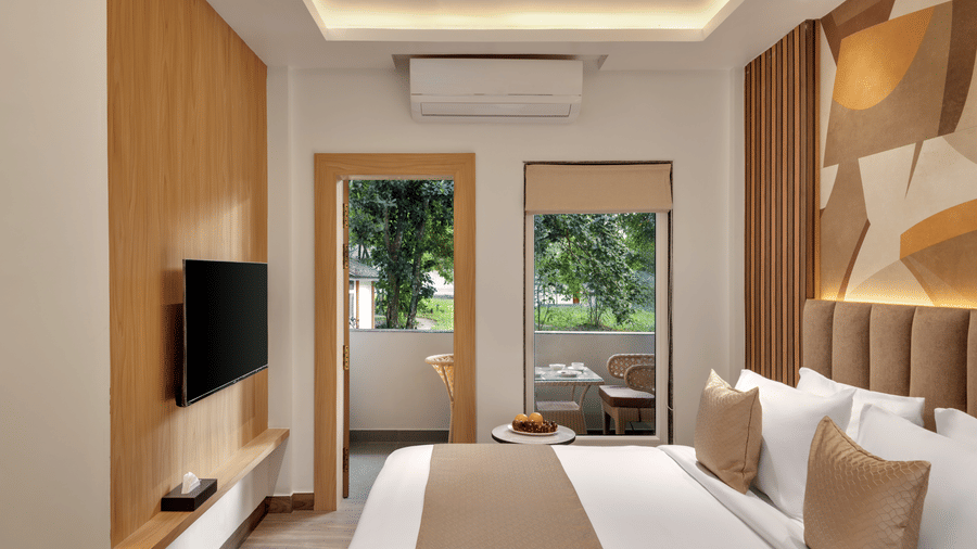 A hotel bedroom with a large double bed, light wood panelling on the walls, recessed lighting, and two glass doors opening to a view of trees outside | Voyage Eastin Suites