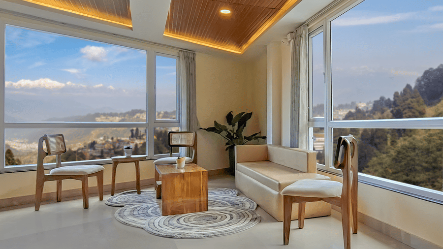A lounge area with a sofa, wooden chairs, and panoramic views of the misty mountains | Voyage Rodhi Resort
