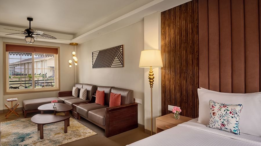 A hotel room featuring a king size bed with a wood-panelled headboard, a patterned rug, and a seating area with a sofa and coffee table. A large window provides natural light - Voyage The Solitaire Bliss.