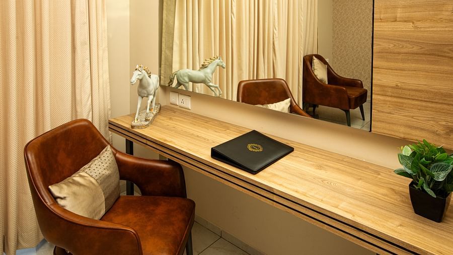 Hotel corner with a chair, a wall-mounted mirror, and a horse statue on a shelf