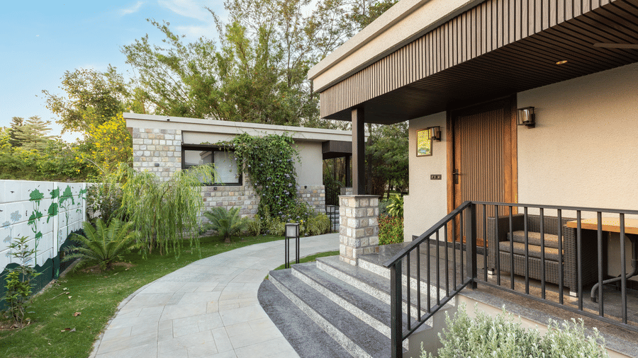 Exterior of jungle spring villa with curved stone pathway leading up to the entrance of a building with stairs and metal railing  at The Golden Tusk, Jim Corbett