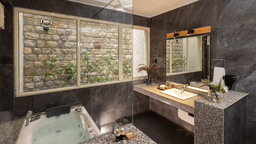 bathroom with a spacious vanity area, a white bathtub, and a large window and decorative panel above the tub area  at The Golden Tusk, Jim Corbett