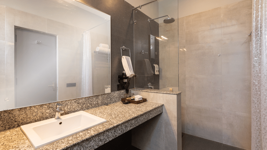  Bathroom with a single marble-top vanity, a large mirror, and a glass-enclosed walk-in shower area at The Golden Tusk, Jim Corbett