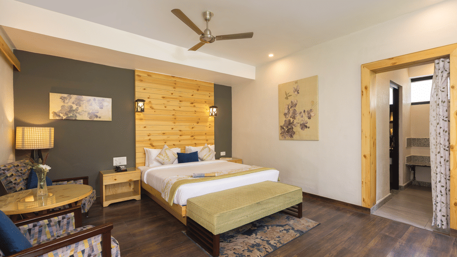 A bedroom with a large bed, wooden flooring, a ceiling fan, and an open doorway