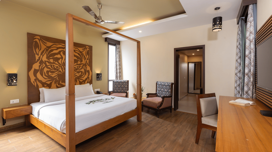 A bedroom with a wooden bed with furniture and a doorway leading into another section of the room at The Golden Tusk, Jim Corbett