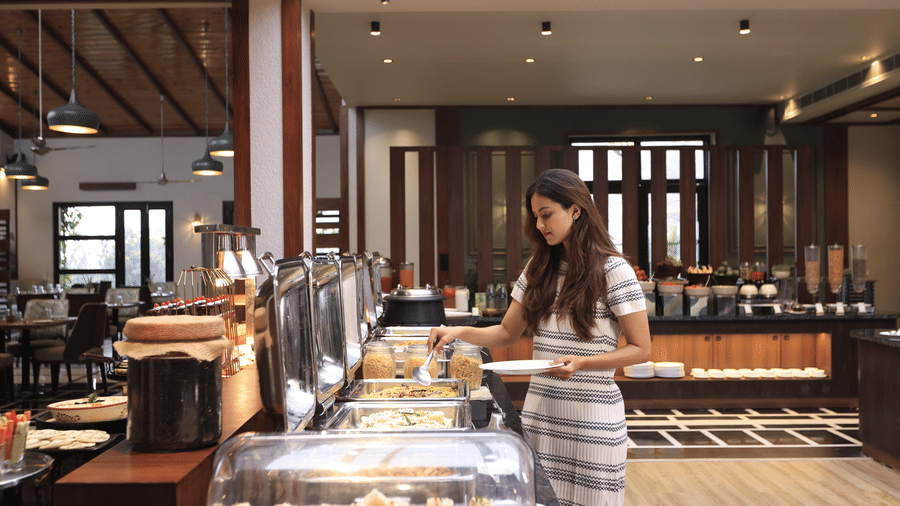 An interior of dining area, featuring a buffet counter and a women serving herself at The Golden Tusk, Jim Corbett