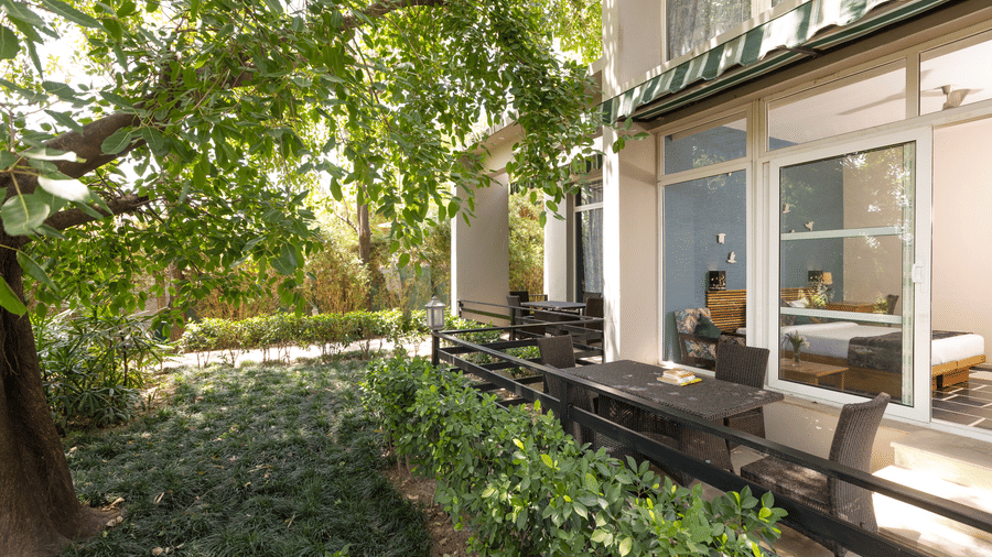 Exterior of nature view suite with large glass windows, a patio, and surrounding greenery at The Golden Tusk, Jim Corbett