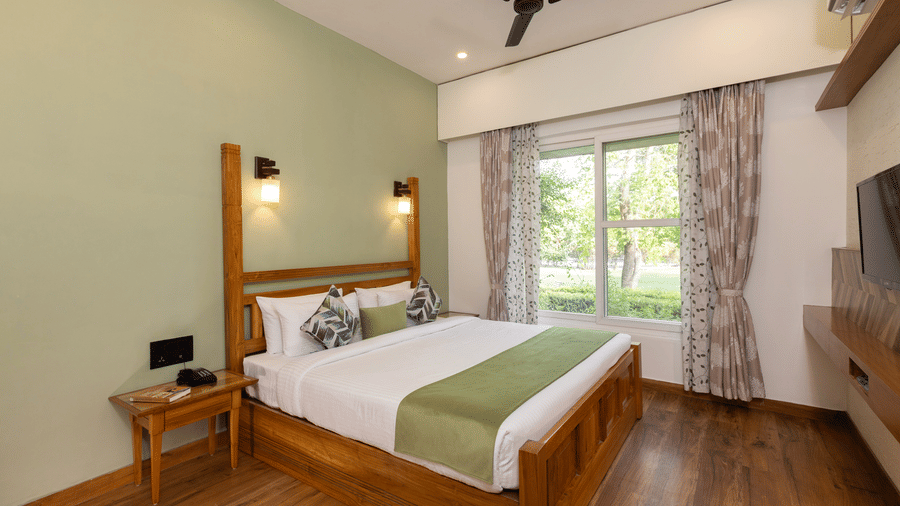 Garden Suite featuring a wooden bed frame, white and green bedding, and a ceiling fan at The Golden Tusk, Jim Corbett