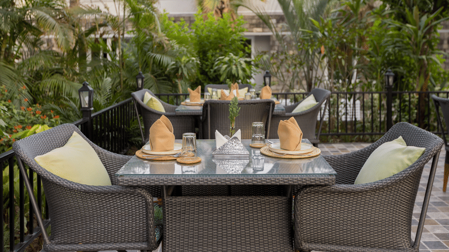 A set outdoor dining table with two chairs and cushions, surrounded by dense plants and trees at The Golden Tusk, Jim Corbett