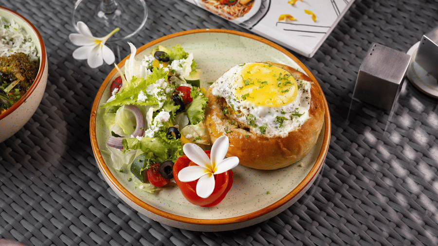Plate of food, including eggs, greens, and a small flower garnish, on a table at The Golden Tusk, Jim Corbett 