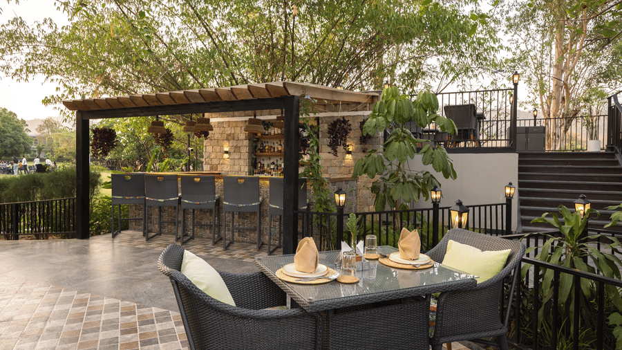 An outdoor dining area with modern dark furniture, wooden pergolas, and trees in the background  at The Golden Tusk, Jim Corbett