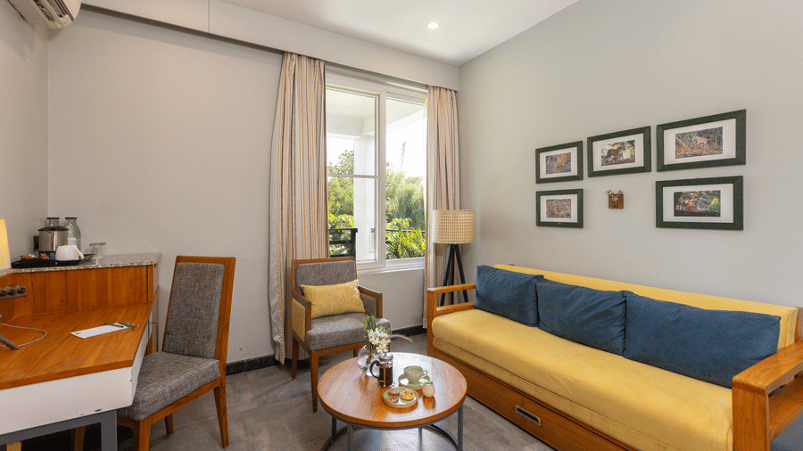 Pool View Suite with a couch, dining table, chairs, and framed pictures on the wall at The Golden Tusk, Jim Corbett