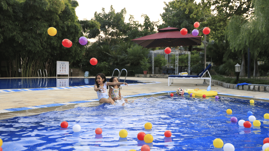 A lively swimming pool filled with colorful balloons and people swimming and playing, surrounded by trees  at The Golden Tusk, Jim Corbett