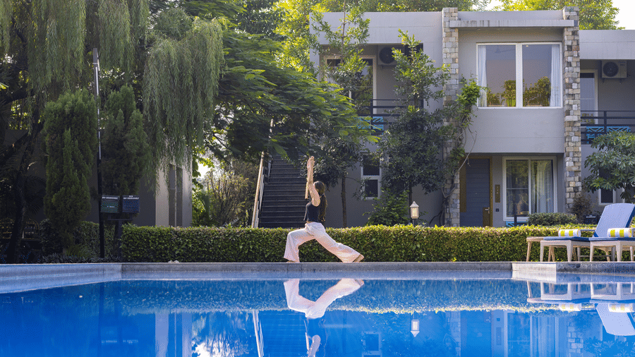 A person stretching  by the edge of a swimming pool with modern buildings and trees behind them at The Golden Tusk, Jim Corbett