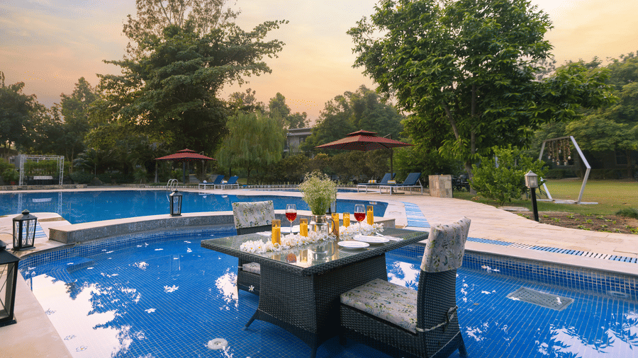 A swimming pool with a table and chairs set up near the water, illuminated by warm light at The Golden Tusk, Jim Corbett