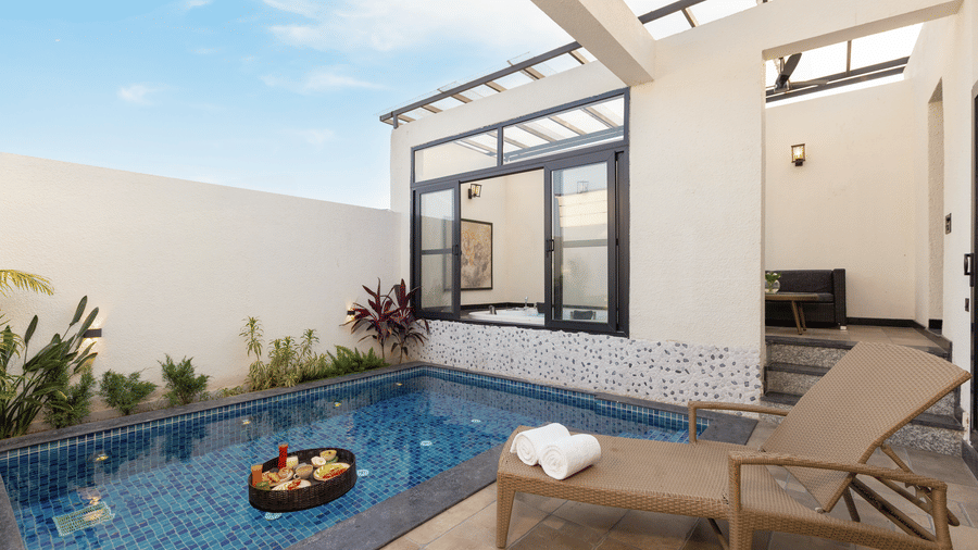 Waterhole Private Pool Villa Private area featuring a swimming pool with a floating tray of fruits, a lounge chair with towels, and modern architecture with a partial glass roof at The Golden Tusk, Jim Corbett