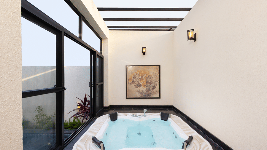 Waterhole Private Pool Villa bathroom interior featuring a large white jacuzzi tub next to floor-to-ceiling windows with an outdoor view at The Golden Tusk, Jim Corbett