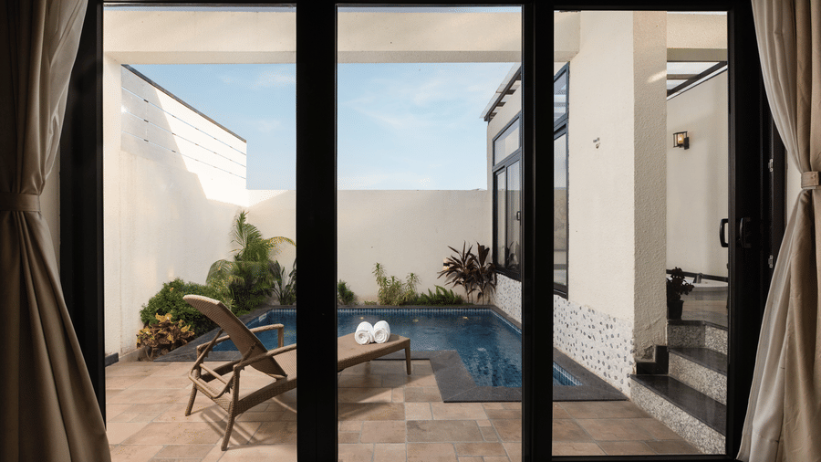 Waterhole Private Pool Villa view through large windows into an outdoor patio area with a small pool, some plants, and a lounge chair at The Golden Tusk, Jim Corbett