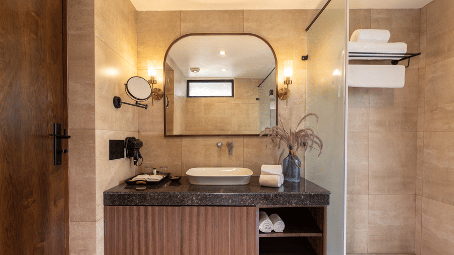 Waterhole Private Pool Villa bathroom featuring a wooden vanity cabinet, a white sink, an arched mirror with side lighting, and a glass shower partition at The Golden Tusk, Jim Corbett