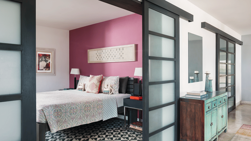 A bedroom at Owl and the Pussycat Hotel in Galle with a bed, patterned flooring, sliding glass doors, and an adjoining sitting area.