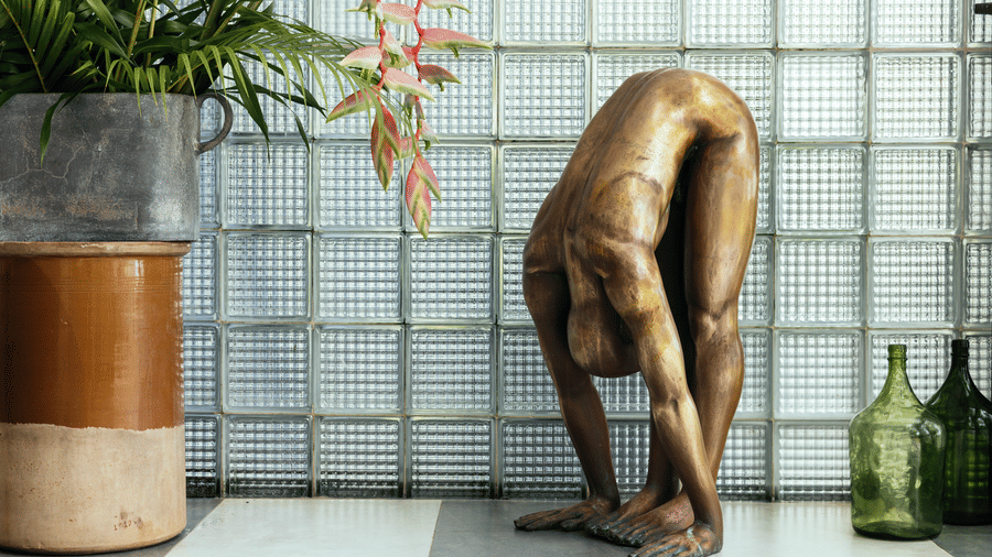 A decorative sculpture placed against a textured glass wall with indoor plants nearby at Owl and the Pussycat Hotel in Galle.