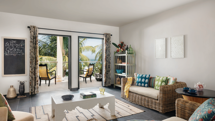 A bright living room at Owl and the Pussycat Hotel in Galle with sofas, cushions, indoor plants, and large glass doors opening to a balcony.
