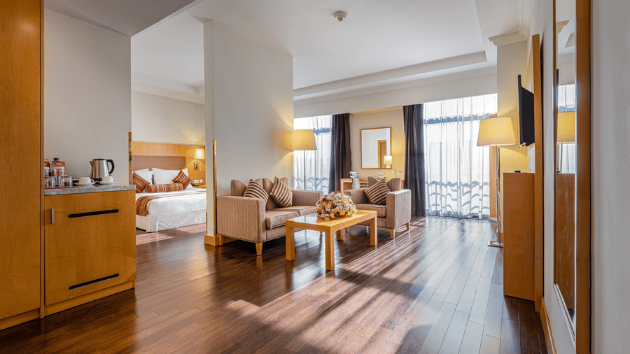Spacious suite at Ramada by Wyndham Addis, featuring a separate living area with cosy seating, a king size bed, warm wooden flooring, and floor-to-ceiling windows for ample natural light.