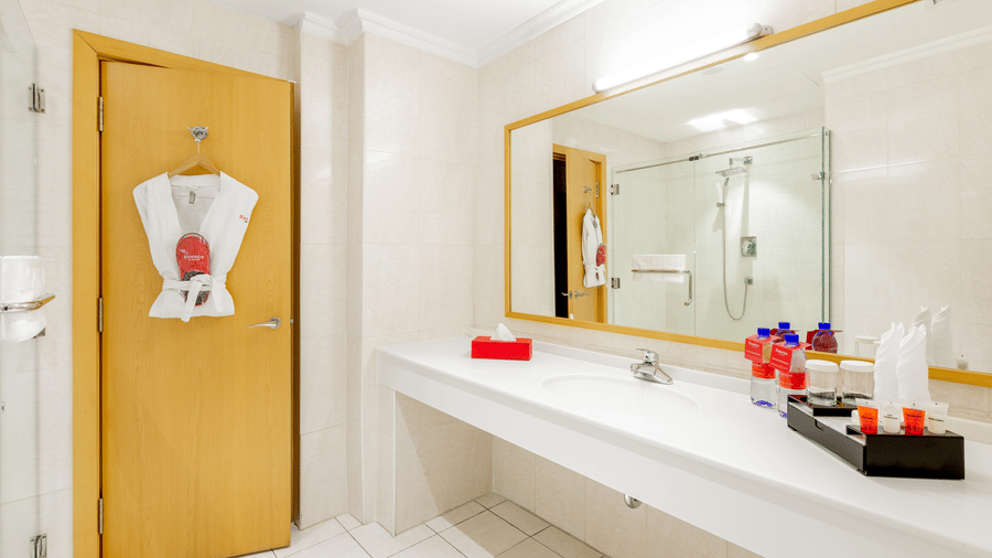 An overview of a bathroom with the sink area in view and a bathrobe hung on the door - Ramada by Wyndham Addis, Addis Ababa.