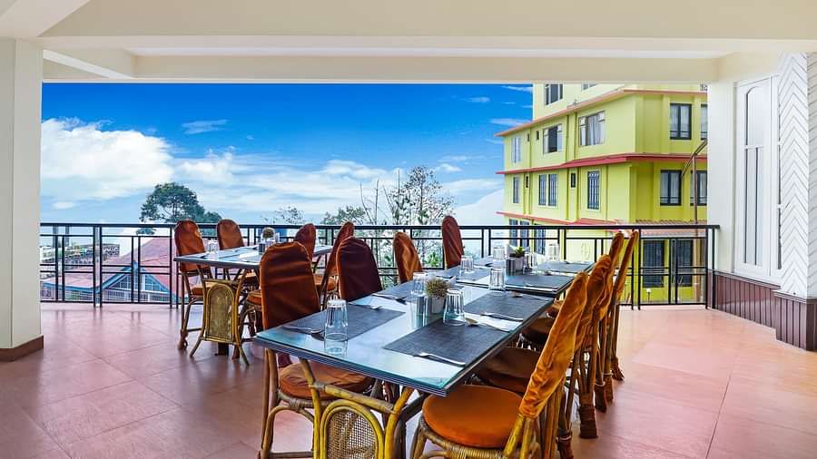 A dining table with multiple chairs placed in the balcony with a backdrop of blue sky | Summit Newa Regency & Spa, Pelling