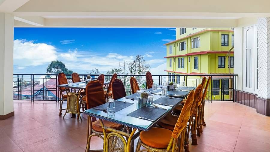 A dining table with multiple chairs placed in the balcony with a backdrop of blue sky | Summit Newa Regency & Spa, Pelling