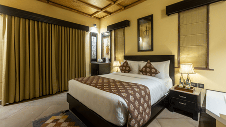 A cosy bedroom at Aamaghati Wildlife Resort with a king size bed, soft lighting, and large windows offering a serene stay.