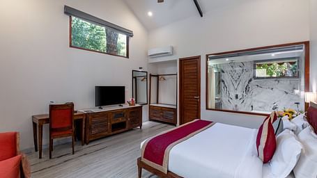 corner view image of the luxury bathtub villa featuring a king size bed along with the glass partition separating the bathroom from the room at aranya vilas in udaipur