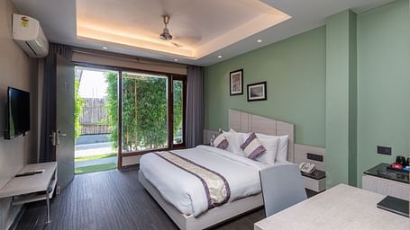 Spacious room at DLS Forest Vines Resort featuring a large bed, a bedside table, a table with chairs, and a large glass door leading to the balcony.