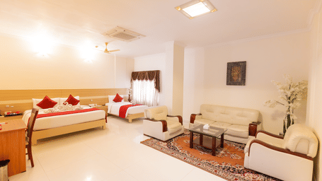 A Suite Room at DSF Grand Plaza, Tuticorin showing the bed area and a cream leather sofa and armchairs arranged around a glass coffee table on a patterned rug.