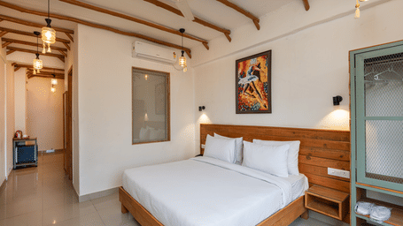 Spacious bedroom with wooden king size bed, artwork, and glass-panelled door at Ekawa Ganga, Rishikesh.