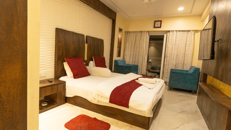 A bedroom with a king size bed, red cushions, a rug, 2 armchairs and a side table at Hotel Seagull Digha.