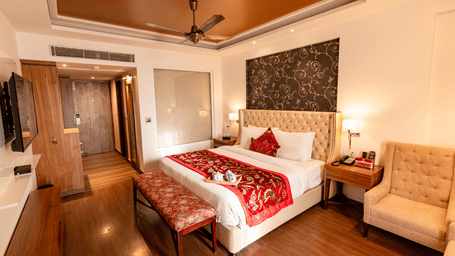 A bedroom with a king size bed, side tables, lamps, wall-mounted TV, armchair, and wardrobe arranged indoors at Indraprastha Resort & Spa, McLeod Ganj.