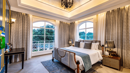 Miros Suite featuring a plush bed facing the TV on the wall, with ample natural light coming from the windows at MIROS Hotels